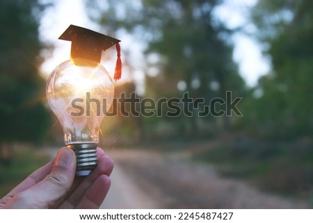 A hand holding a light bulb and graduation cap in front of the sun. Idea of education, technology, use of solar energy
