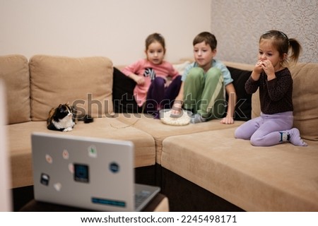  Three children with kitten sitting on the living room watching movie or cartoon from laptop.