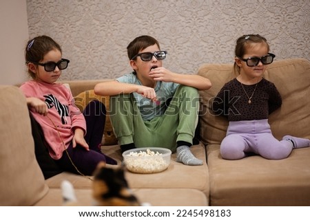  Three children sitting on the living room, wear 3d glasses watching movie or cartoon.