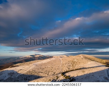 snow covered mountains at sunset with a winding road in the foreground aerial view