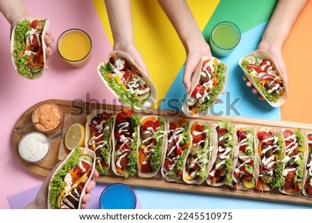 Friends holding delicious tacos on color background, top view