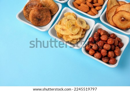 Bowls with dried fruits and nuts on light blue background, above view. Space for text