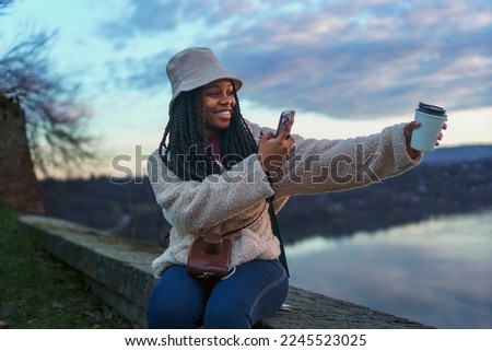 Female black tourist looking at river from a old city fortress, she's drinking coffee and taking pictures of her coffee and the view
