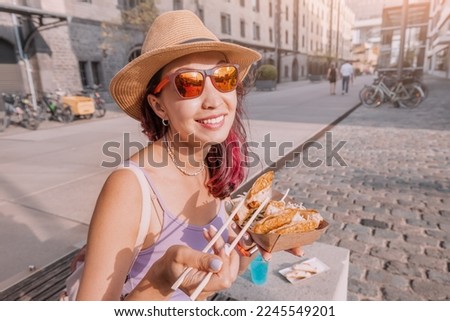 Happy cheerful girl eating spring rolls from takeaway paper box using chopsticks at city street. Fast food eatery and asian cuisine Royalty-Free Stock Photo #2245549201