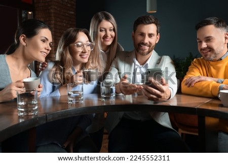 Handsome man showing something funny in smartphone to his friends in cafe