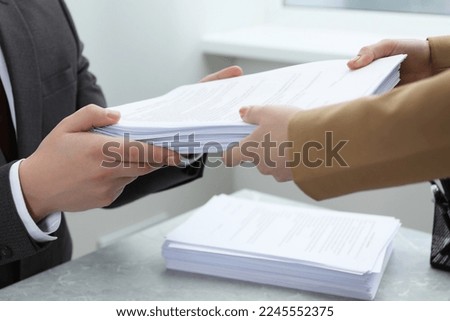Woman giving many documents to man at table in office, closeup