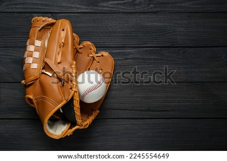 Catcher's mitt and baseball ball on black wooden table, top view with space for text. Sports game