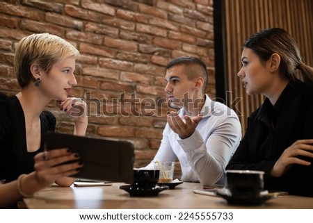 Three young business colleagues having a meeting in a modern cafe in the late evening hours. Successfull startup team analysing data after work hours.