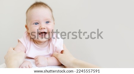 Cute two month old baby on a beige background. Caring for a European small child. The baby looks at his mother and smiles. Mother does gymnastics with the baby. Happy family concept.