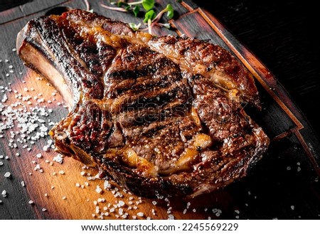 Grilled Ribeye Steak on bones on wooden board, prime cowboy steak on dark background