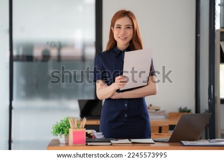 Asian businesswoman arms crossed and holding document paper in an office.