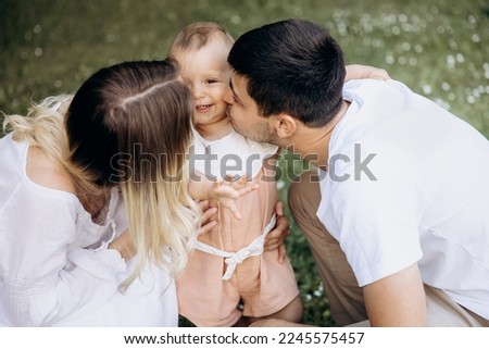 young mother and father play with their little daughter in the countryside outdoors. stylish young family dressed in white with a small child