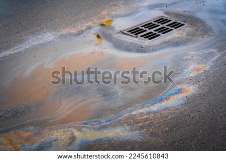 Oil slick on the asphalt road background drains into the storm drain. Water pollution environmental problems. Selective focus. Royalty-Free Stock Photo #2245610843