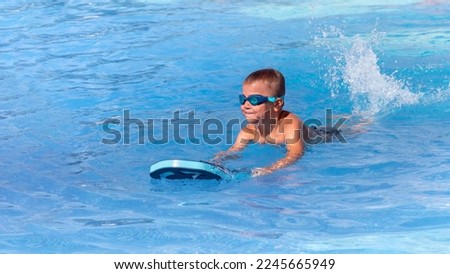 Little boy in swimming goggles with float foam board tool swim in pool in sunny day. Safe pool training, summer holiday, family vacation, travel, water sport concept Royalty-Free Stock Photo #2245665949