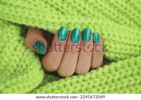 Woman's hand with green and silver manicure on a light background. Stylish fashionable woman's manicure. Nail polish. Artistic manicure. Modern style. Winter manicure.