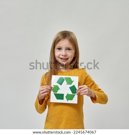 Smiling caucasian little girl holding paper with recycle sign. Ecology safety. Waste disposal and recycling. Environmental sustainability. Isolated on white background. Studio shoot. Copy space