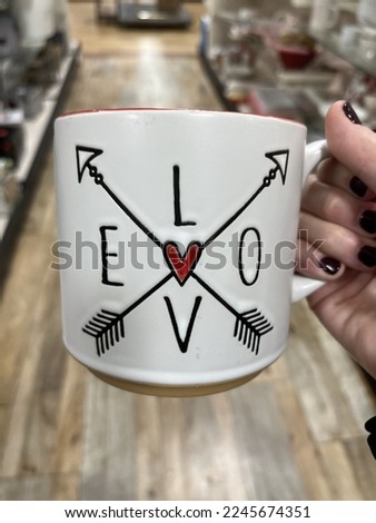 A woman holding a coffee mug that has two arrows and the word love written on it.