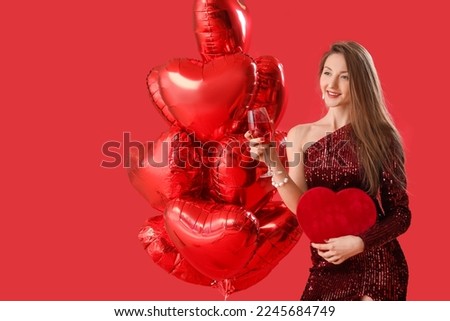 Young woman with glass of wine, gift and balloons on red background. Valentine's Day celebration