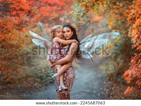 Fantasy woman fairy, holding little girl in her arms. Mom and daughter are hugging, happy face looking at camera. Fairy carnival costumes butterfly wings, shiny pink matching dresses. family shooting Royalty-Free Stock Photo #2245687063
