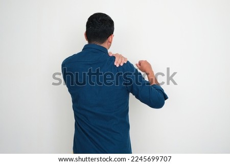 Back view of adult Asian man suffering shoulder pain