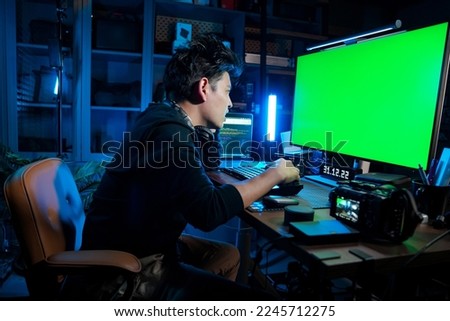 Asian man look at the Green Screen Computer Monitor in the Dark Office. Blue mood and tone.
He looks tired and feels head-edge and very serious. His hand touches his head.