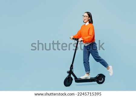 Full body side view cool happy young woman of Asian ethnicity wear orange sweater glasses riding electric scooter isolated on plain pastel light blue cyan background studio People lifestyle concept Royalty-Free Stock Photo #2245715395