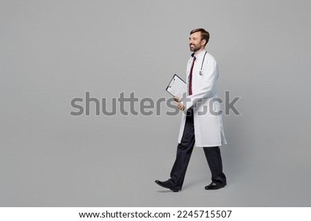 Full body side view male doctor man wears white medical gown suit work in hospital hold clipboard with paper documents walk isolated on plain grey color background studio Healthcare medicine concept Royalty-Free Stock Photo #2245715507