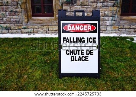 Close up of a danger falling ice warning sign board in both English and French near building. Winter safety concept.