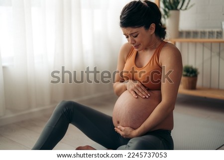 Pregnant woman is feeling contractions, desperately trying to ease the pain she's feeling while waiting the emergency to come. Royalty-Free Stock Photo #2245737053