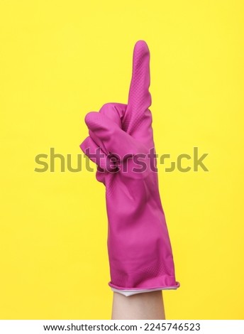 Hand in purple rubber cleaning glove point index finger up on a yellow background. House cleaning and housekeeping concept