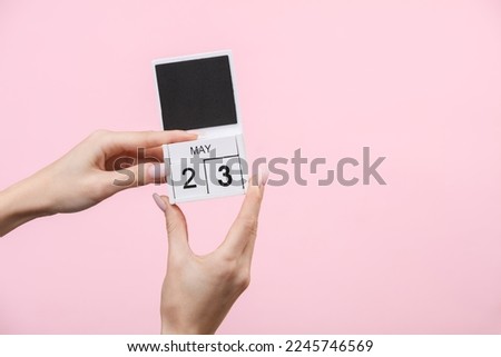 Block calendar with date may 23 in female hands on pink background