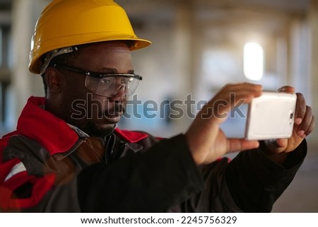 Worker taking photo on smartphone. Builder at construction site filming videos. African american worker records videos on smartphone