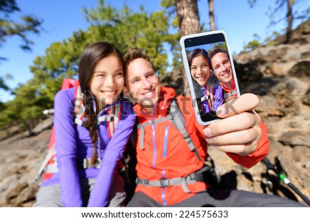 Selfie couple using smart phone hiking in nature with smartphone. Happy couple taking self-portrait photo picture using app. Man and woman having fun together. Focus on screen.