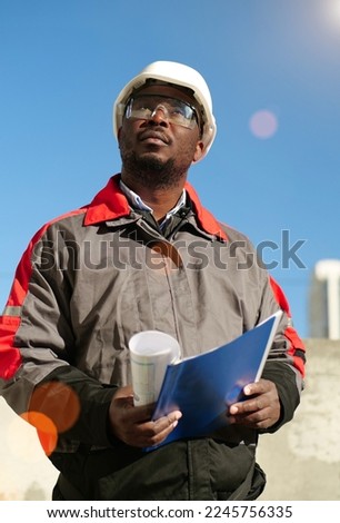 African american worker stands at construction site, holds in hands work papers and looks forward