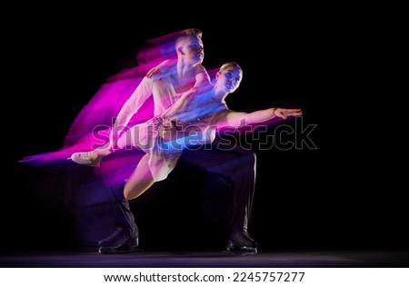 Portrait of artistic man and woman, figure skating athletes dancing isolated on black background in neon with mixed lights. Concept of movement, sport, beauty, hobby, competition, dance, choreography