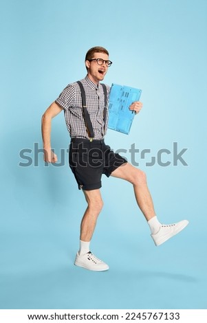 Portrait of young man in checkered shirt, shorts and suspenders with laptop isolated over blue background. Successful project. Concept of emotions, business, education, occupation, facial expression
