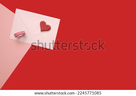 Valentine's Day themed flat lay with a pink love letter, white envelope, red heart, and decorative Love You tape.