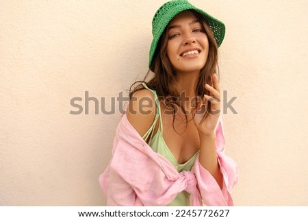 Beautiful young caucasian woman looking at camera wide smiling during summer day. Model with brunette wavy hair wears shirt and sundress. Concept of great mood. Royalty-Free Stock Photo #2245772627