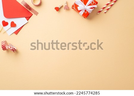 Valentine's Day concept. Top view photo of red giftbox envelope with paper sheet straws hearts decorative tape and clips on isolated pastel beige background with empty space