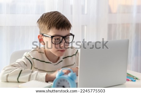 Alarm clock with back to school supplies in background. Learn concepts with boy holding clock on computer laptop.