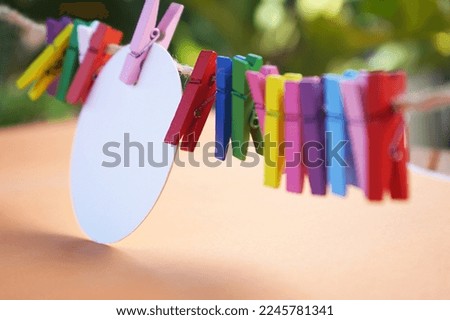 Colorful background of wooden paper clips and white circle label paper on rope, on soft orange and green bokeh light background. Copy space for creative design.