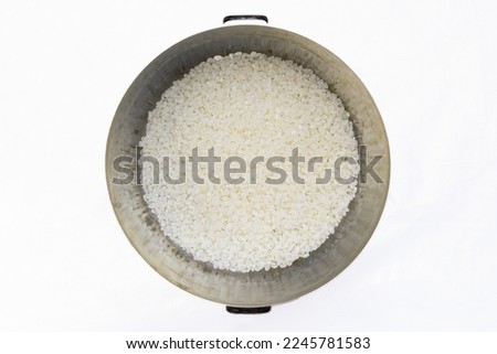 Pan with white rice inside, top view, on a white background. Uncooked food, kitchen tools Royalty-Free Stock Photo #2245781583