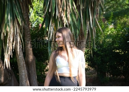 Young, pretty, blonde, blue-eyed woman strolling through the park and posing for the photo like a model. She is happy doing different body postures and expressions.