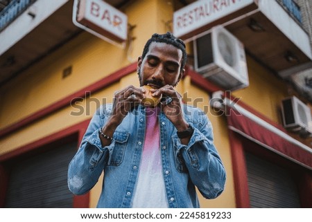 Portrait of a man biting a delicious burger because he is really hungry. He is outside in the city. Royalty-Free Stock Photo #2245819233