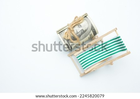 Flatlay picture of folding beach chair with roll of fake money on isolated white background.