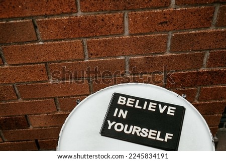 Believe in Yourself message on black paper lying on a table with brick wall background. Motivational inspirational modern message concept.