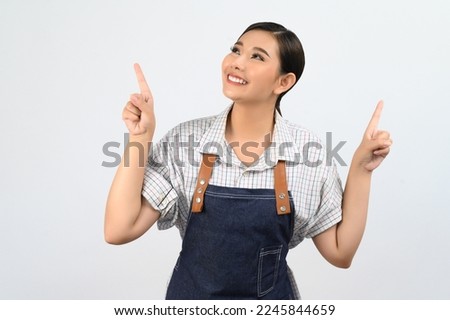 Portrait Asian young woman smile with happy in waitress uniform and apron, Cheerful girl standing with hand signal, point finger isolated on white background