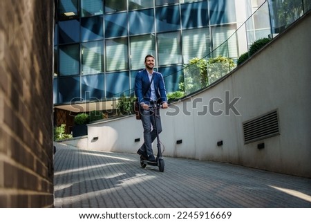 Young business man in a suit riding an electric scooter on a business meeting. Ecological transportation concept Royalty-Free Stock Photo #2245916669