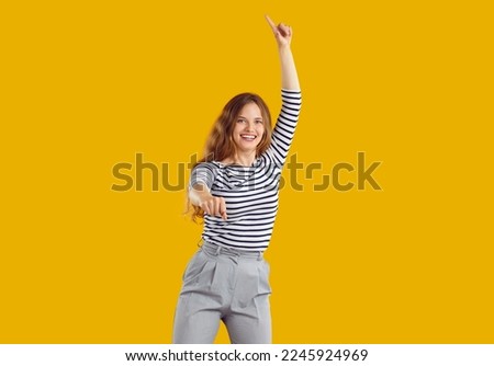 Funny woman dancing in studio. Portrait of happy energetic beautiful lively young girl in striped top and grey trousers dancing and jumping isolated on yellow colour background
