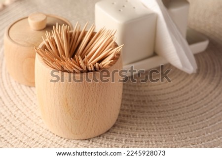 Wooden holder with many toothpicks on wicker mat, closeup. Space for text Royalty-Free Stock Photo #2245928073